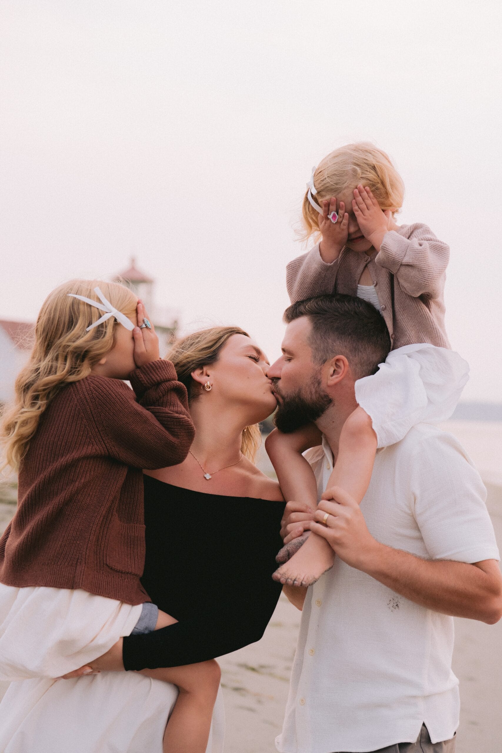 A family of four on the beach, with parents kissing and two children covering their eyes.