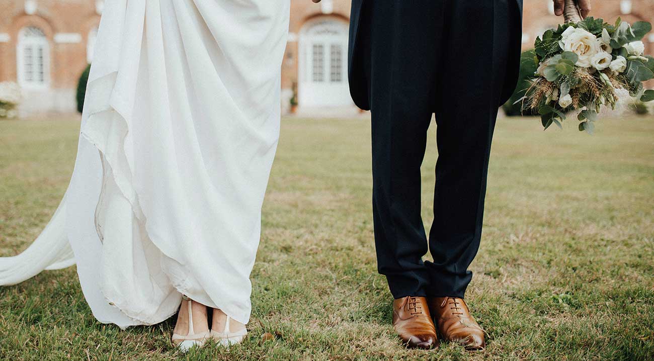 Close-up of bride's dress and groom's suit standing on grass at a wedding.